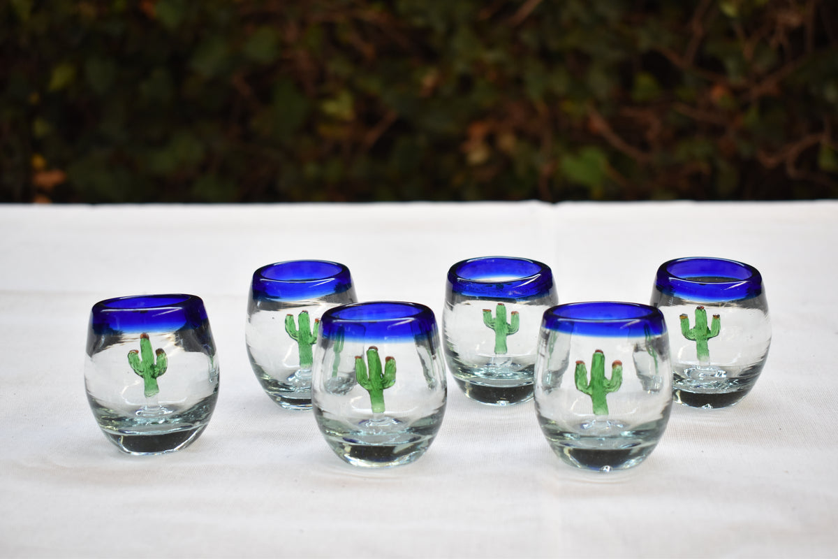 Handblown shot glasses with cobalt blue rims and cactus details on a table